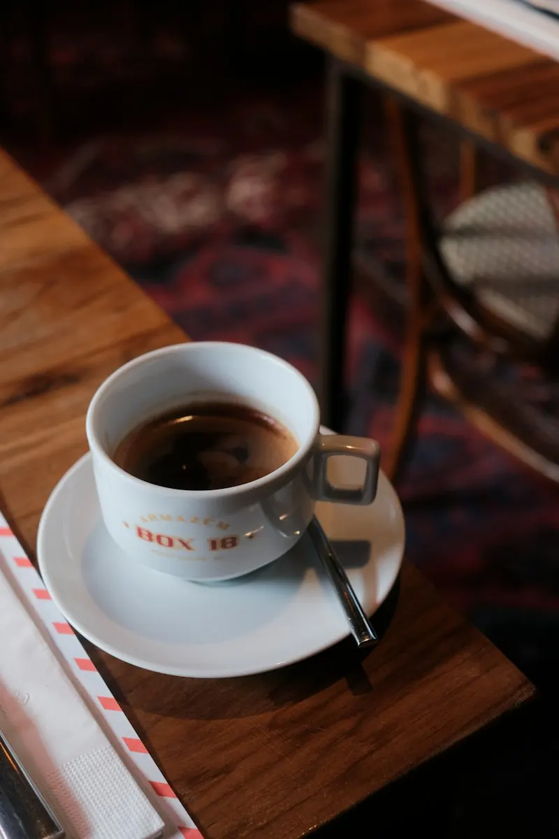 En kopp svart kaffe på fat på ett mörkt träbord.